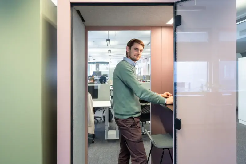 Man smiling inside a rose-colored Vetrospace XS+ pod while working at a standing desk.