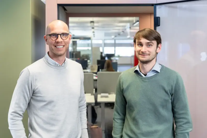 Two men smiling in front of a Vetrospace pod in a modern office setting.