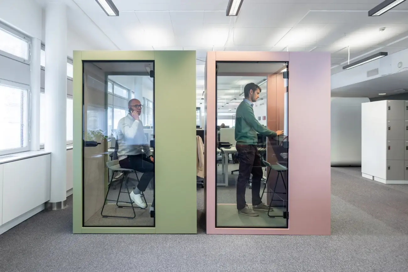 Two Vetrospace pods in olive green and rose pink, each with an employee working inside.