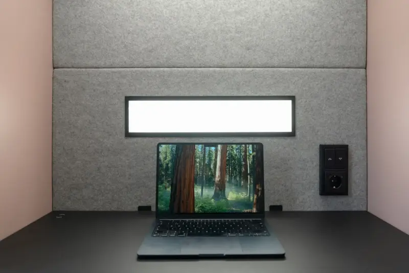Close-up view of a laptop displaying a forest image inside a Vetrospace pod with a built-in light and wall outlets.