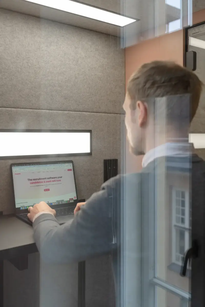 Man working on a laptop inside a soundproof Vetrospace pod with a soft grey interior.