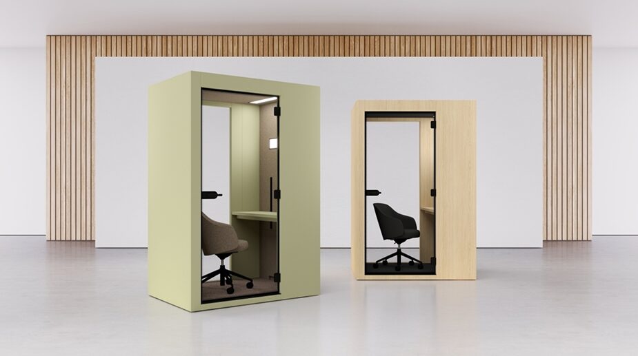 A a showroom space with two compact, soundproof solo work pods—one in a soft green tone and the other in natural oak—each containing an office chair and desk for focused tasks.
